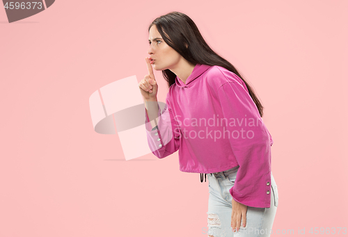 Image of The young woman whispering a secret behind her hand over pink background