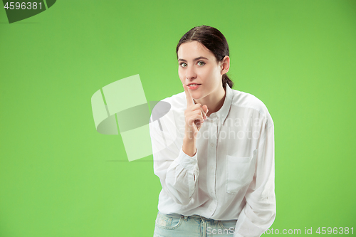 Image of The young woman whispering a secret behind her hand over green background