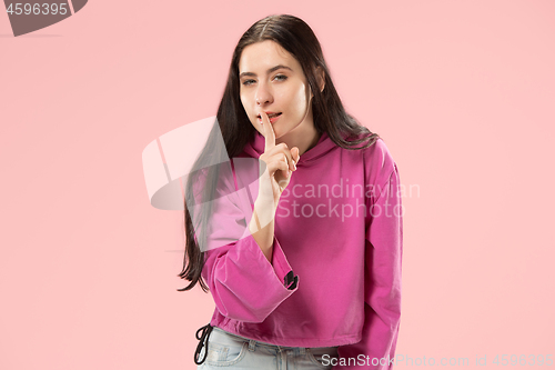 Image of The young woman whispering a secret behind her hand over pink background