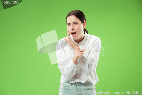 Image of The young woman whispering a secret behind her hand over green background