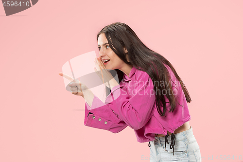 Image of The young woman whispering a secret behind her hand over pink background