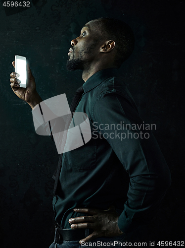 Image of Studio shot of young serious black African man thinking while talking on mobile phone against black background