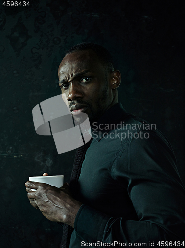 Image of Stylish young black man with cup of coffee posing on dark background.