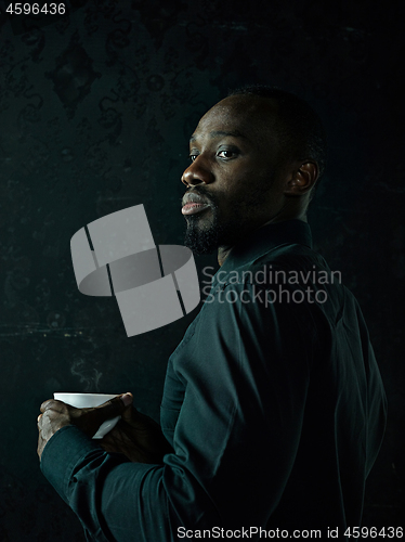 Image of Stylish young black man with cup of coffee posing on dark background.