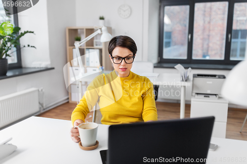 Image of businesswoman with laptop drinks coffee at office