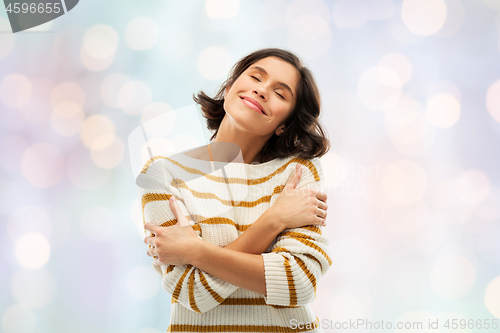 Image of happy woman in striped pullover hugging herself