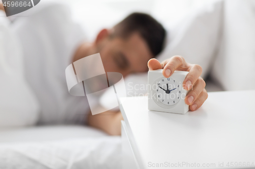 Image of close up of man in bed reaching for alarm clock