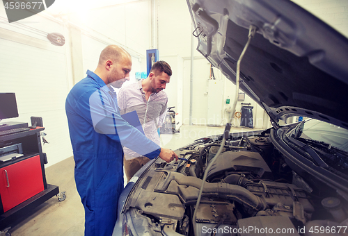 Image of auto mechanic with clipboard and man at car shop