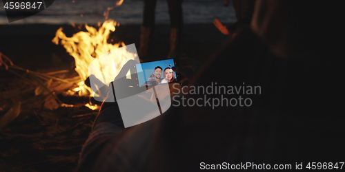 Image of Couple taking photos beside campfire on beach