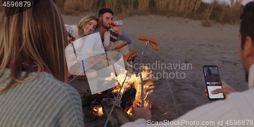 Image of Group Of Young Friends Sitting By The Fire at beach