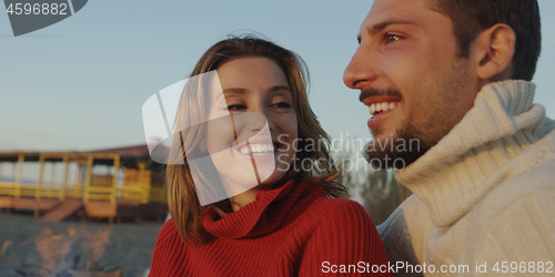 Image of Loving Young Couple Sitting On The Beach beside Campfire drinkin