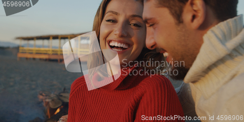 Image of Loving Young Couple Sitting On The Beach beside Campfire drinkin