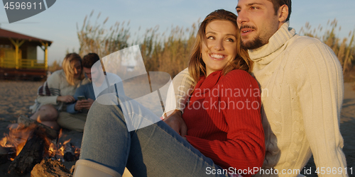 Image of Loving Young Couple Sitting On The Beach beside Campfire drinkin