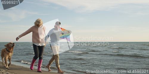 Image of couple with dog having fun on beach on autmun day