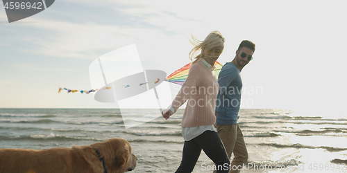 Image of couple with dog having fun on beach on autmun day