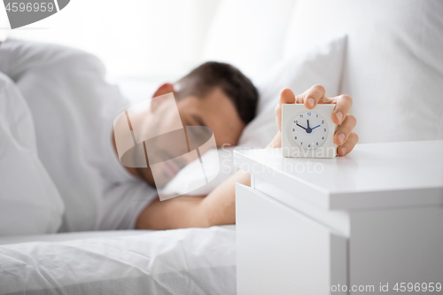 Image of close up of man in bed reaching for alarm clock