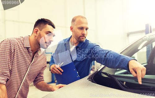 Image of auto mechanic with clipboard and man at car shop