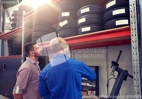 Image of mechanic and man choosing tires at car shop