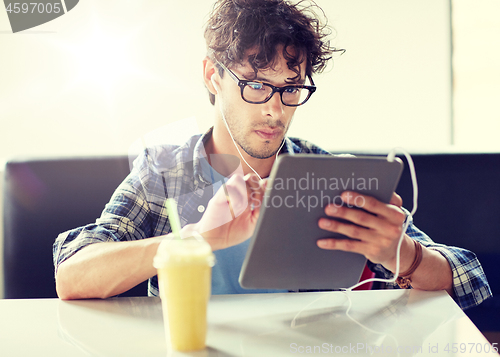 Image of man with tablet pc and earphones sitting at cafe