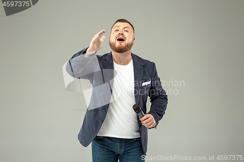 Image of Young man with microphone on gray background, leading with microphone