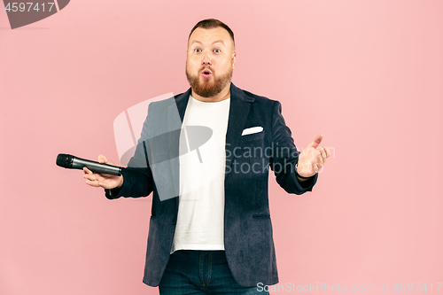 Image of Young man with microphone on pink background, leading with microphone