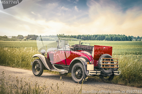 Image of Antique red car on a road in a countryside landscape