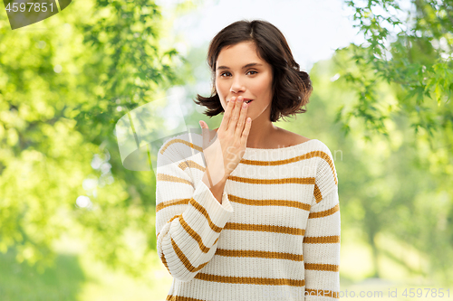 Image of woman covers mouth by hand over natural background
