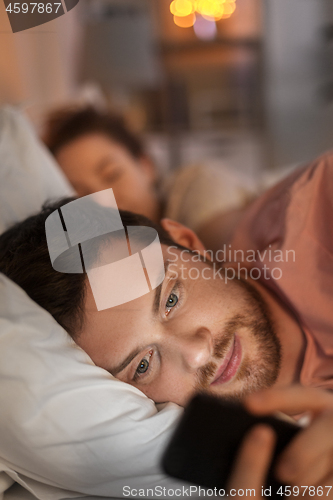 Image of man using smartphone while girlfriend is sleeping