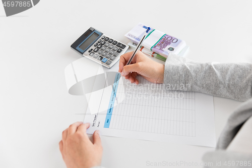 Image of hands with tax form, calculator and money on table