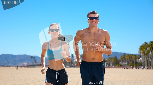 Image of couple in sports clothes running along on beach