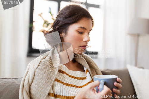 Image of sad sick young woman drinking hot tea at home