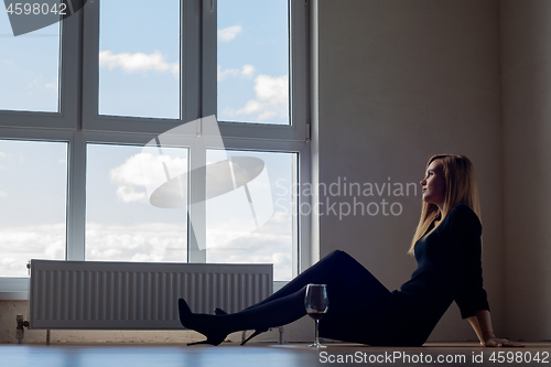 Image of Sad girl with sitting on the floor of an empty room with a glass of wine