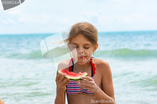 Image of A girl eats a watermelon on the beach