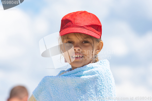 Image of Portrait of a girl in a red cap wrapped in a towel against the sky