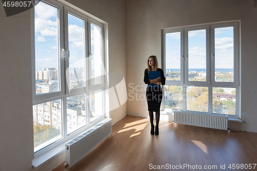 Image of Girl realtor with a folder stands at the big windows of a spacious apartment