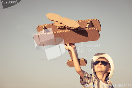 Image of Little boy playing with cardboard toy airplane in the park at th