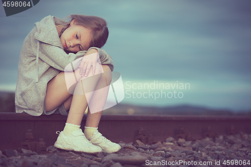 Image of Portrait of young sad girl sitting outdoors  on the railway