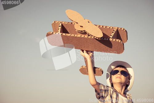 Image of Little boy playing with cardboard toy airplane in the park at th