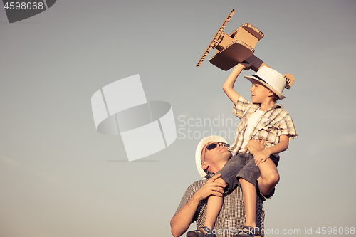 Image of Father and son playing with cardboard toy airplane in the park a