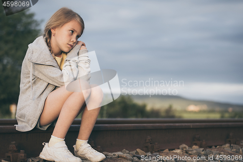 Image of Portrait of young sad girl sitting outdoors  on the railway