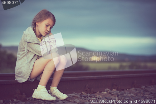 Image of Portrait of young sad girl sitting outdoors  on the railway