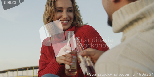 Image of Loving Young Couple Sitting On The Beach beside Campfire drinkin