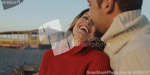 Image of Loving Young Couple Sitting On The Beach beside Campfire drinkin