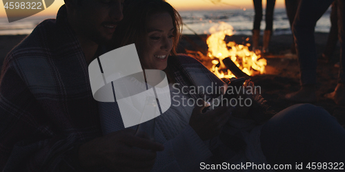 Image of Couple enjoying bonfire with friends on beach