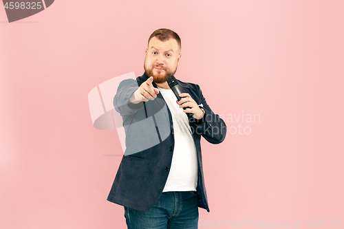 Image of Young man with microphone on pink background, leading with microphone