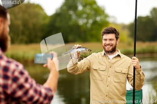 Image of friend photographing fisherman with fish at lake