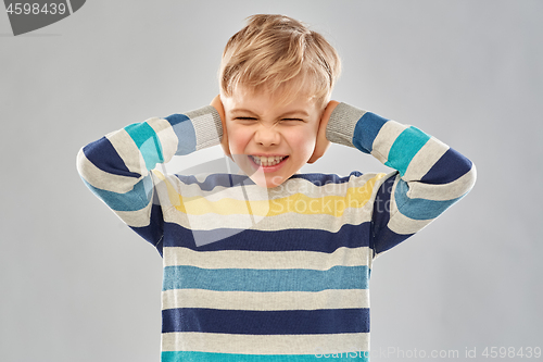 Image of stressed boy in pullover closing ears by hands