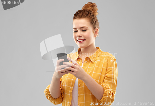 Image of smiling red haired teenage girl using smartphone