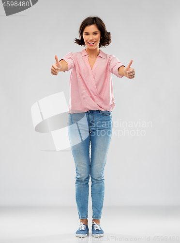 Image of young woman in shirt and jeans showing thumbs up