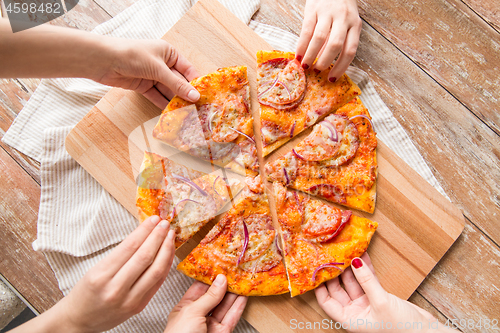 Image of close up of hands sharing pizza on wooden table